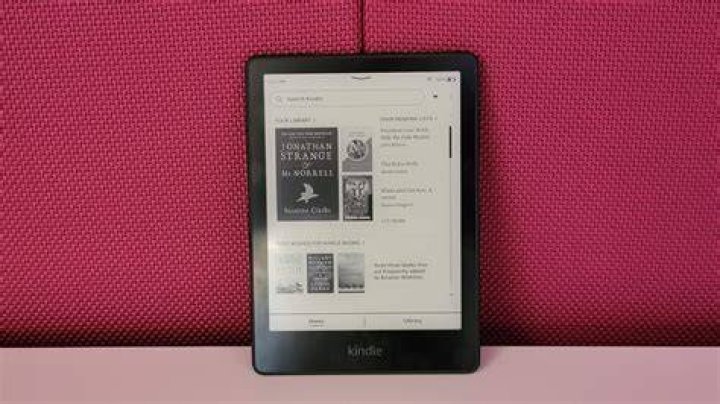 Amazon Kindle Paperwhite 2021 with the screen showing a book cover, on a table, next to a cup of coffee