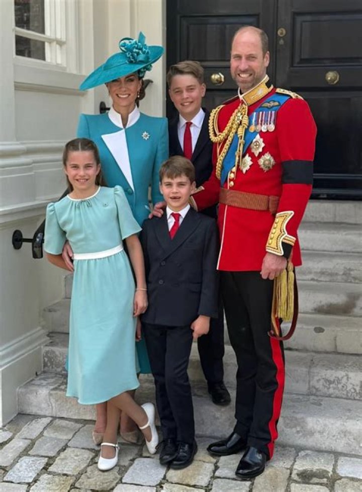 Prince William, a white man with blonde hair wearing a suit, and Kate Middleton, a white woman with a red dress and hat, staring in a royal manner.