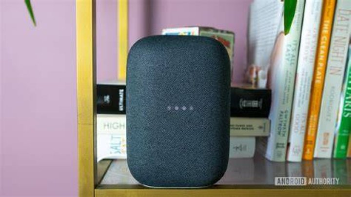 The gray Google Nest Audio speaker pictured on a white desk in front of computer screens.